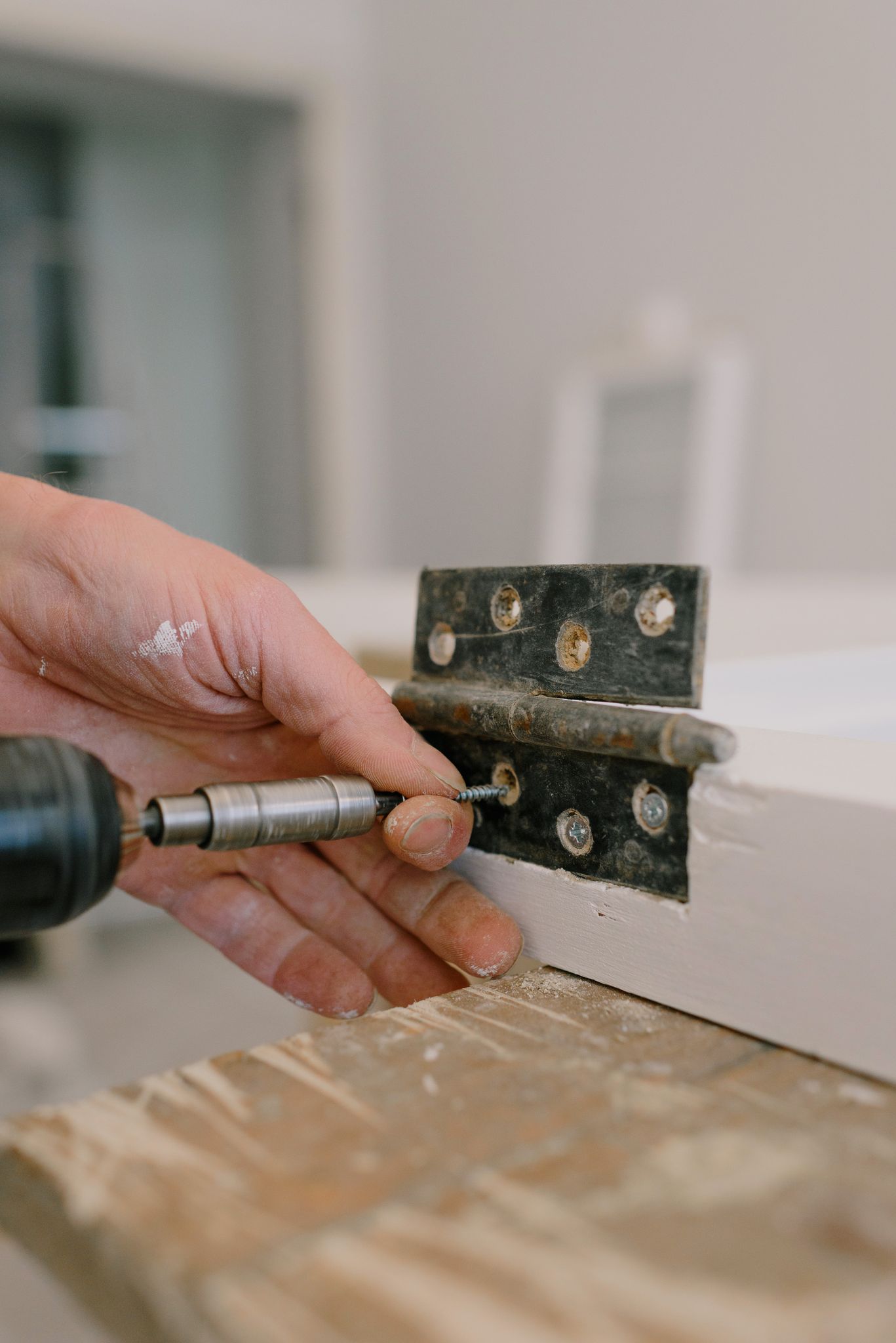 Unrecognizable professional male carpenter using screwdriver to attach metal hinge on window in room with blurred background during renovation works